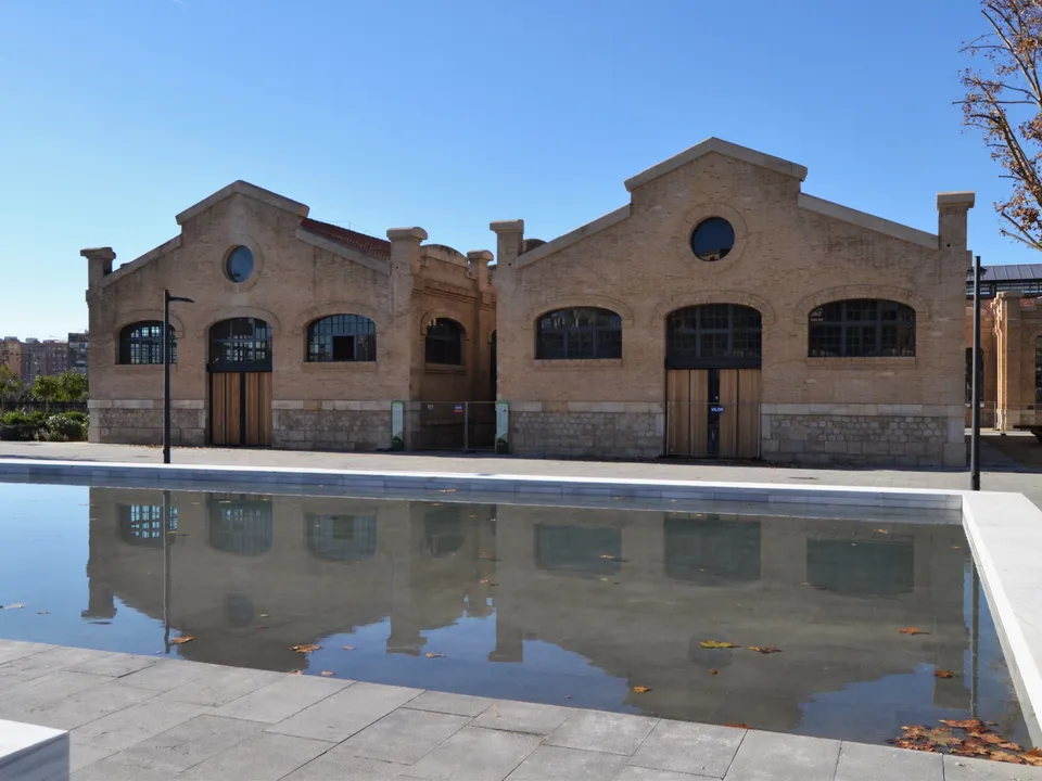 Restored brick railway buildings reflected in a pond at Parc Central, Valencia.